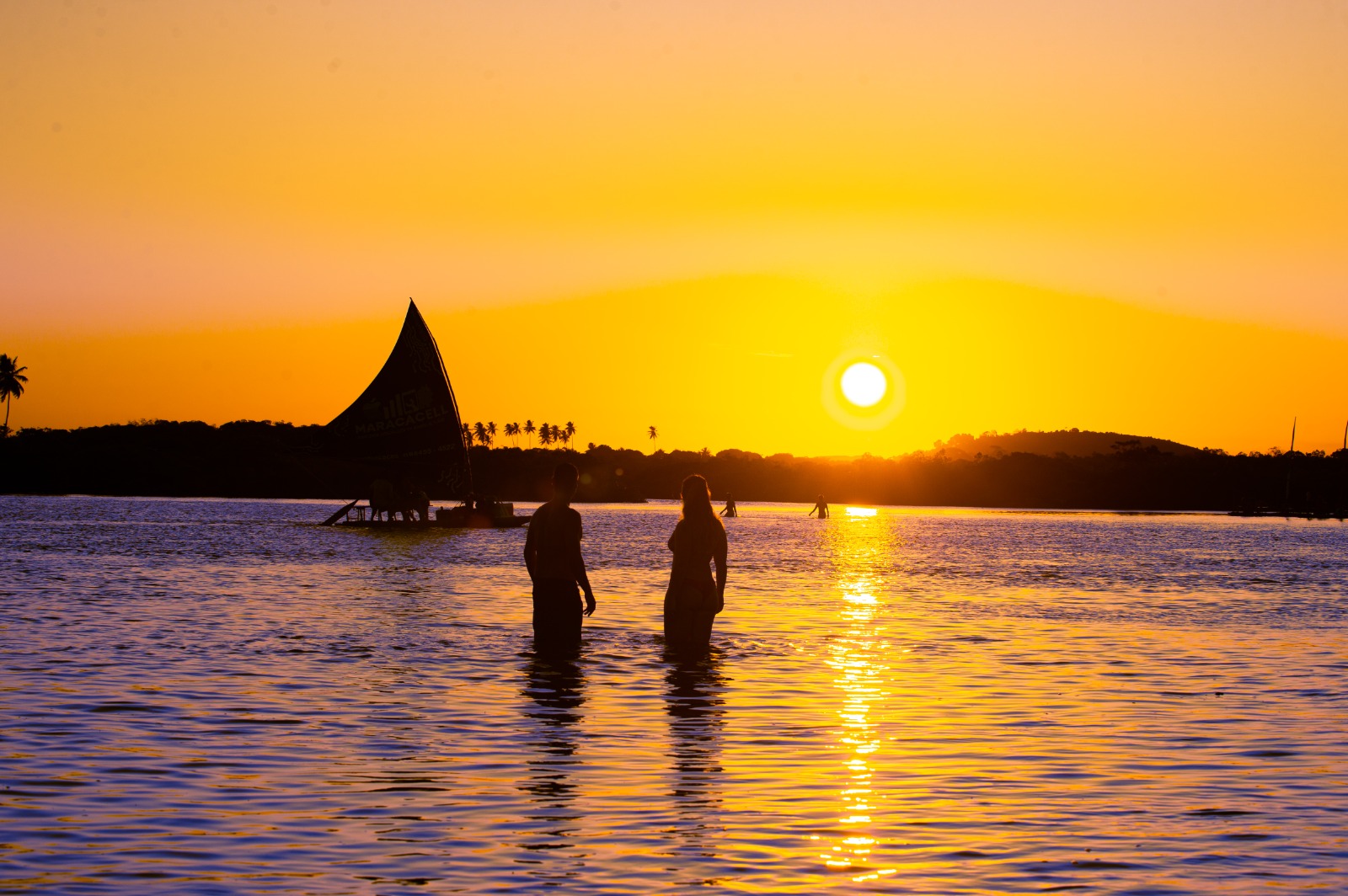 Casal admirando o pôr do sol no Pontal de Maracaípe com jangada ao fundo