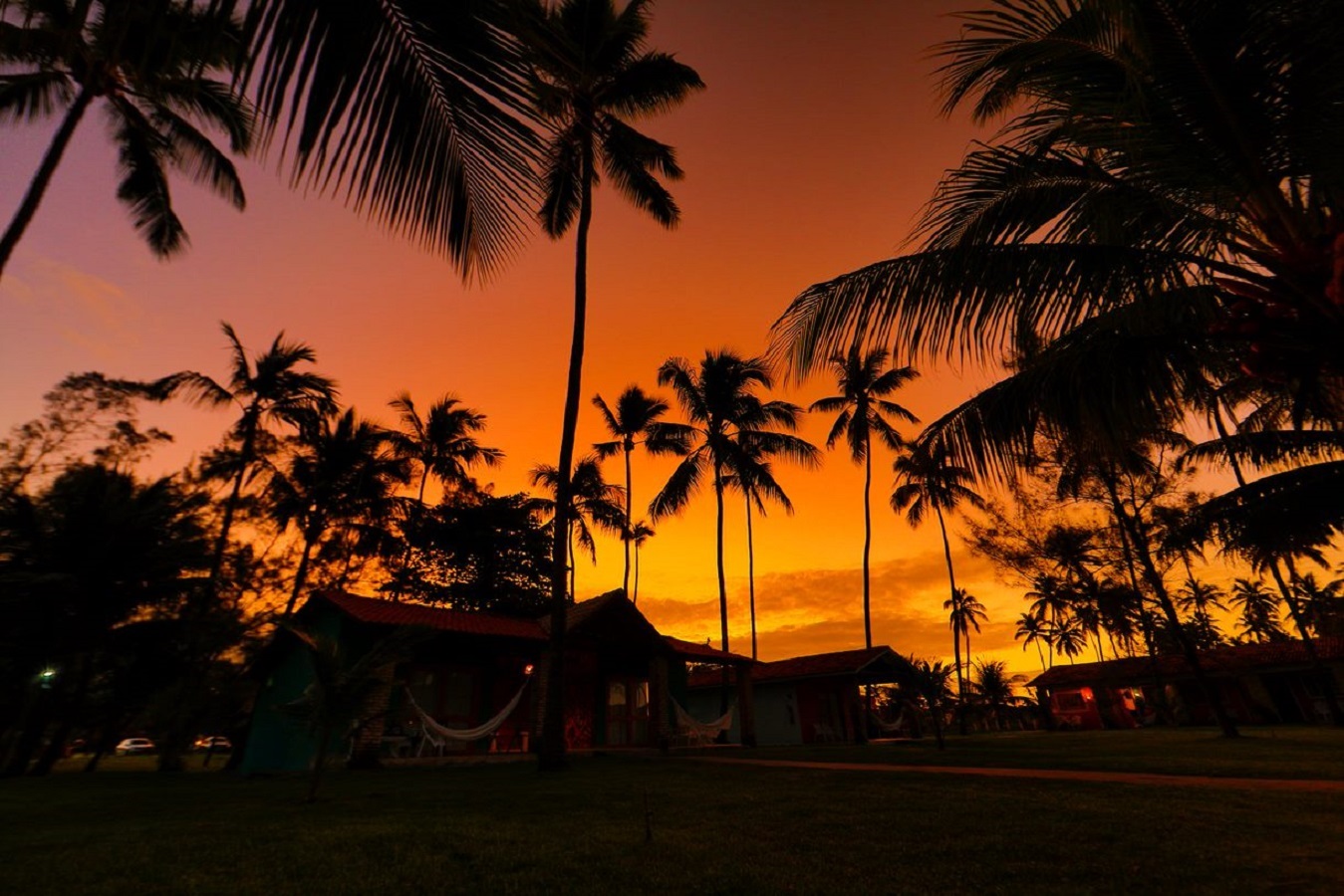 Pôr do sol entre coqueiros e chalés da pousada