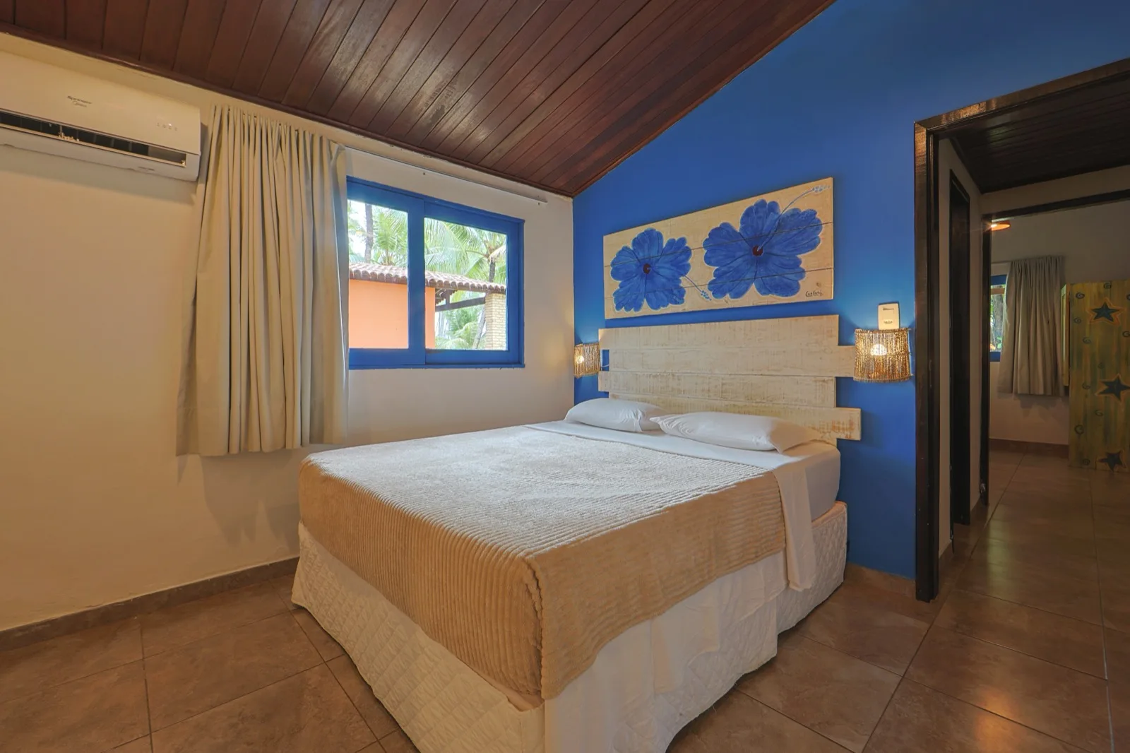 Suíte com cama de casal, parede azul e painel floral, com janela para o jardim