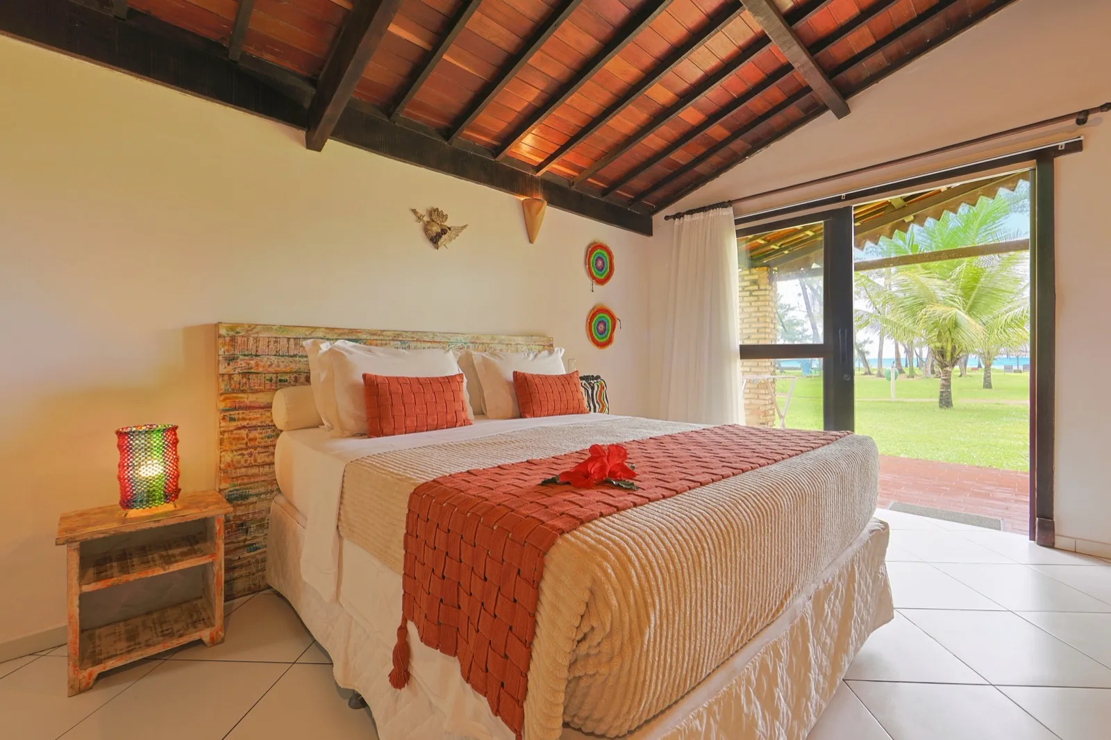 Suíte principal com cama de casal, cabeceira de madeira de demolição e porta corrediça aberta para o jardim e o mar