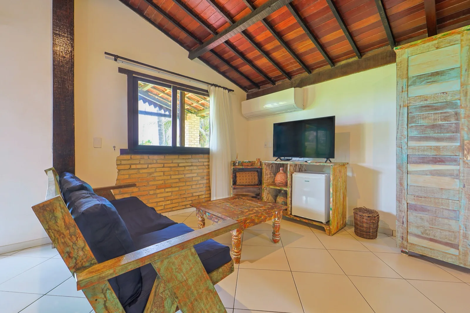 Sala de estar com sofá de madeira de demolição, TV, ar-condicionado e armário rústico colorido