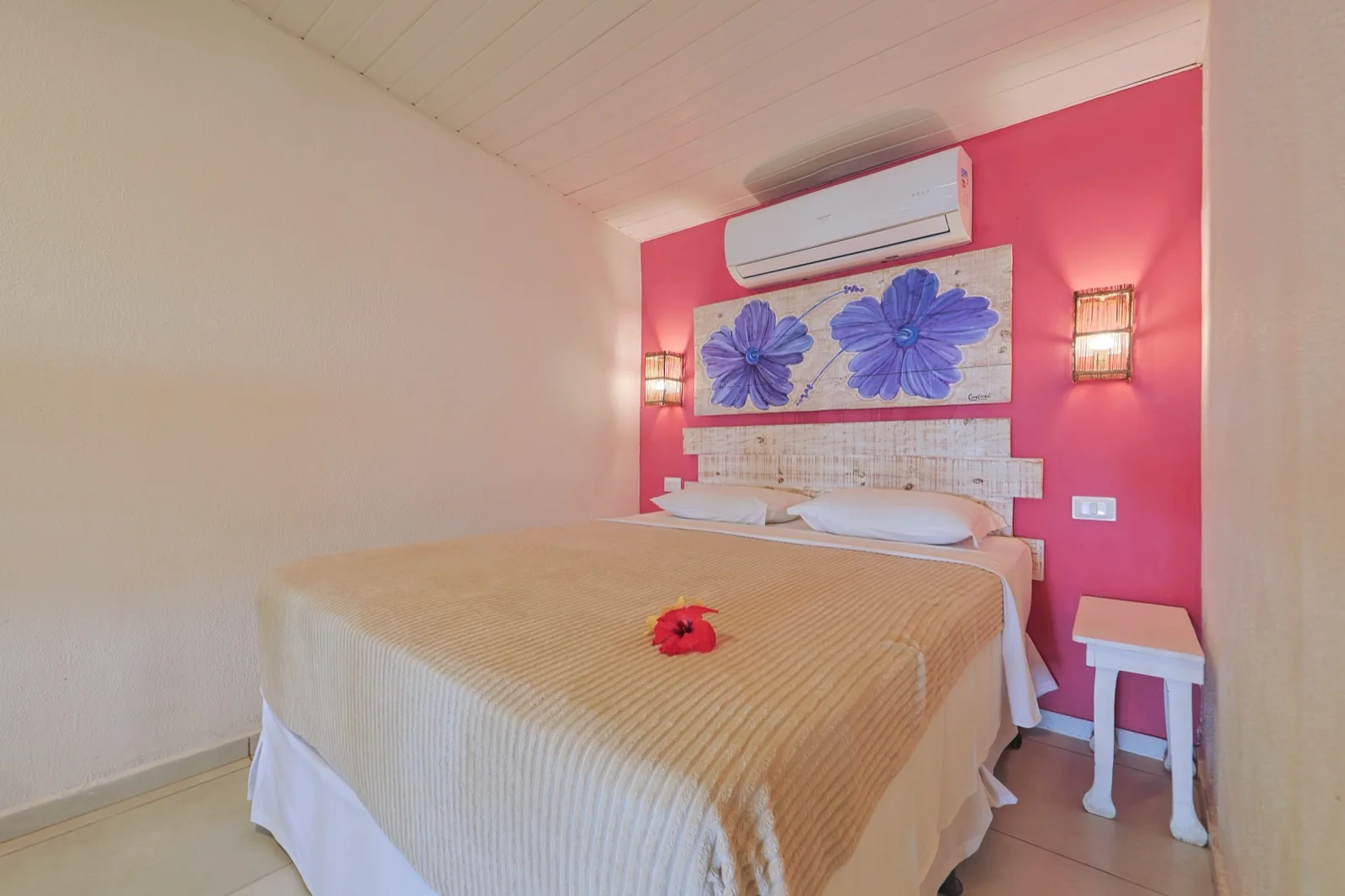 Quarto de casal com parede rosa, painel de flores lilás e hibisco sobre a cama
