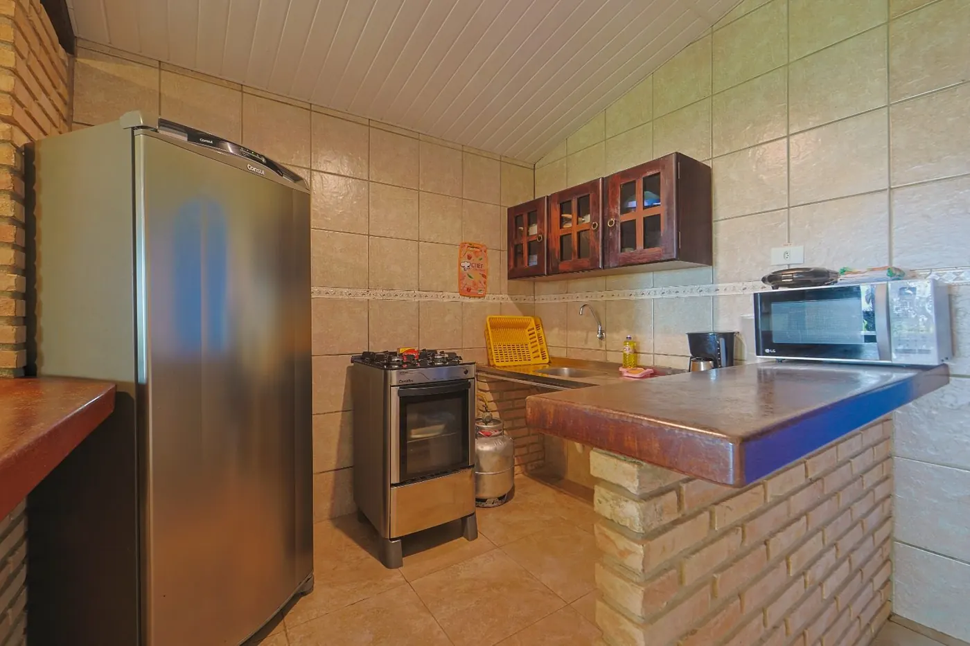 Cozinha equipada com fogão, geladeira, micro-ondas e bancada em madeira