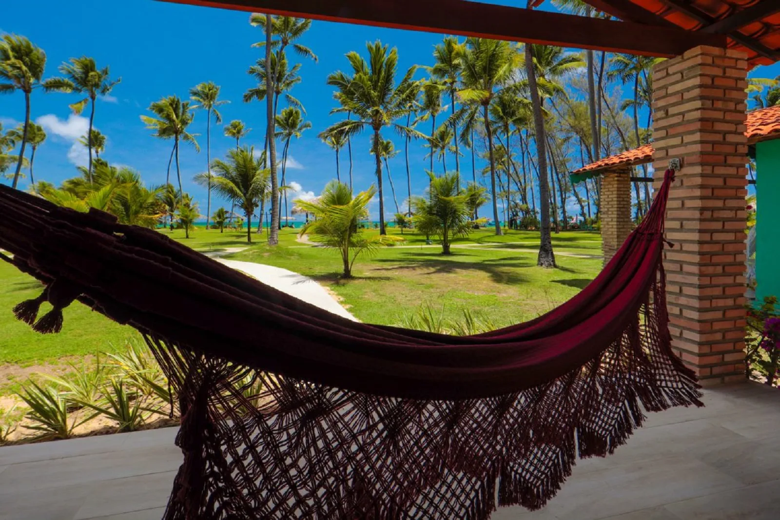 Rede na varanda com vista para o jardim, coqueiros e o mar ao fundo