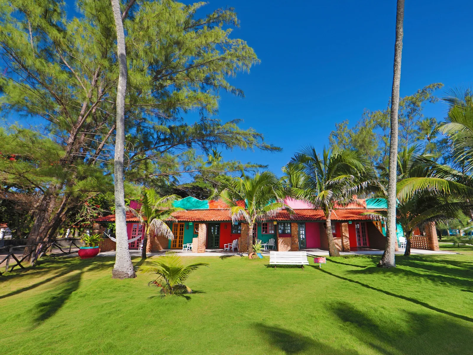 Fachada das suítes Família Vista Mar com telhados coloridos, jardim amplo e coqueiros altos