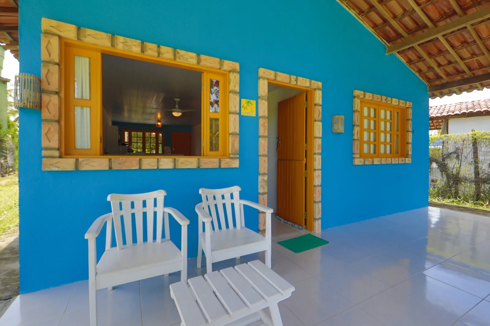 Casa Haras, varanda azul com poltronas brancas e porta laranja de entrada