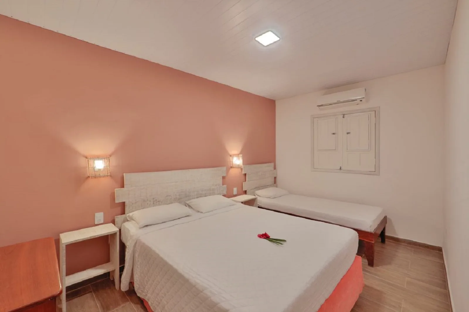 Família Econômico, quarto com cama de casal e solteiro, parede coral e janela com venezianas