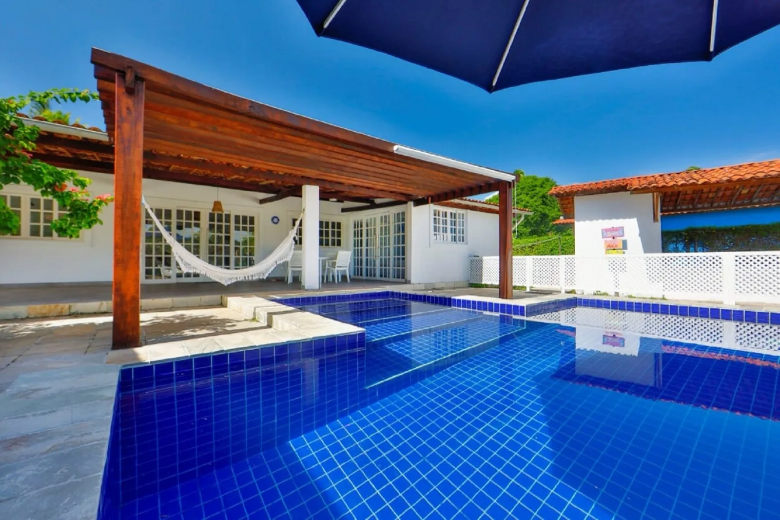 Villa com Piscina Privativa, piscina de azulejo azul-cobalto com pergolado de madeira, rede e fachada branca ao fundo