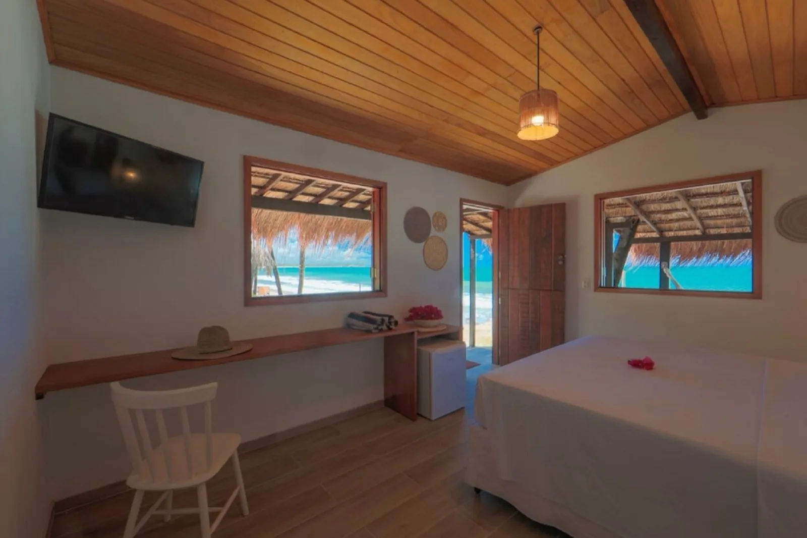 Quarto da Cabana do Mar com TV, cama de casal e janelas emolduradas por palhoça com vista para o mar