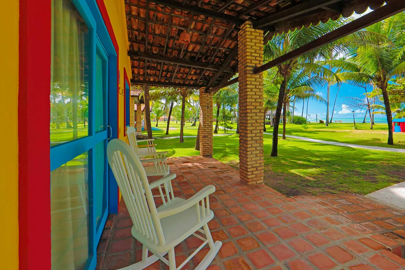 Varanda da casa em piso de tijolo com cadeiras de balanço e vista para o mar