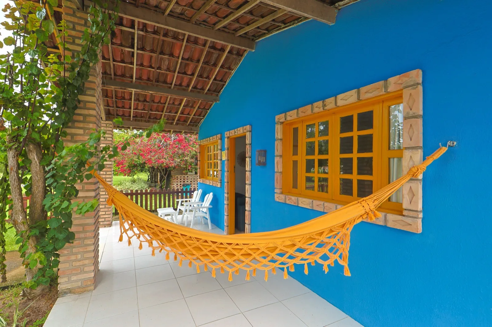 Casa Haras, varanda com rede laranja entre a parede azul e a área verde florida