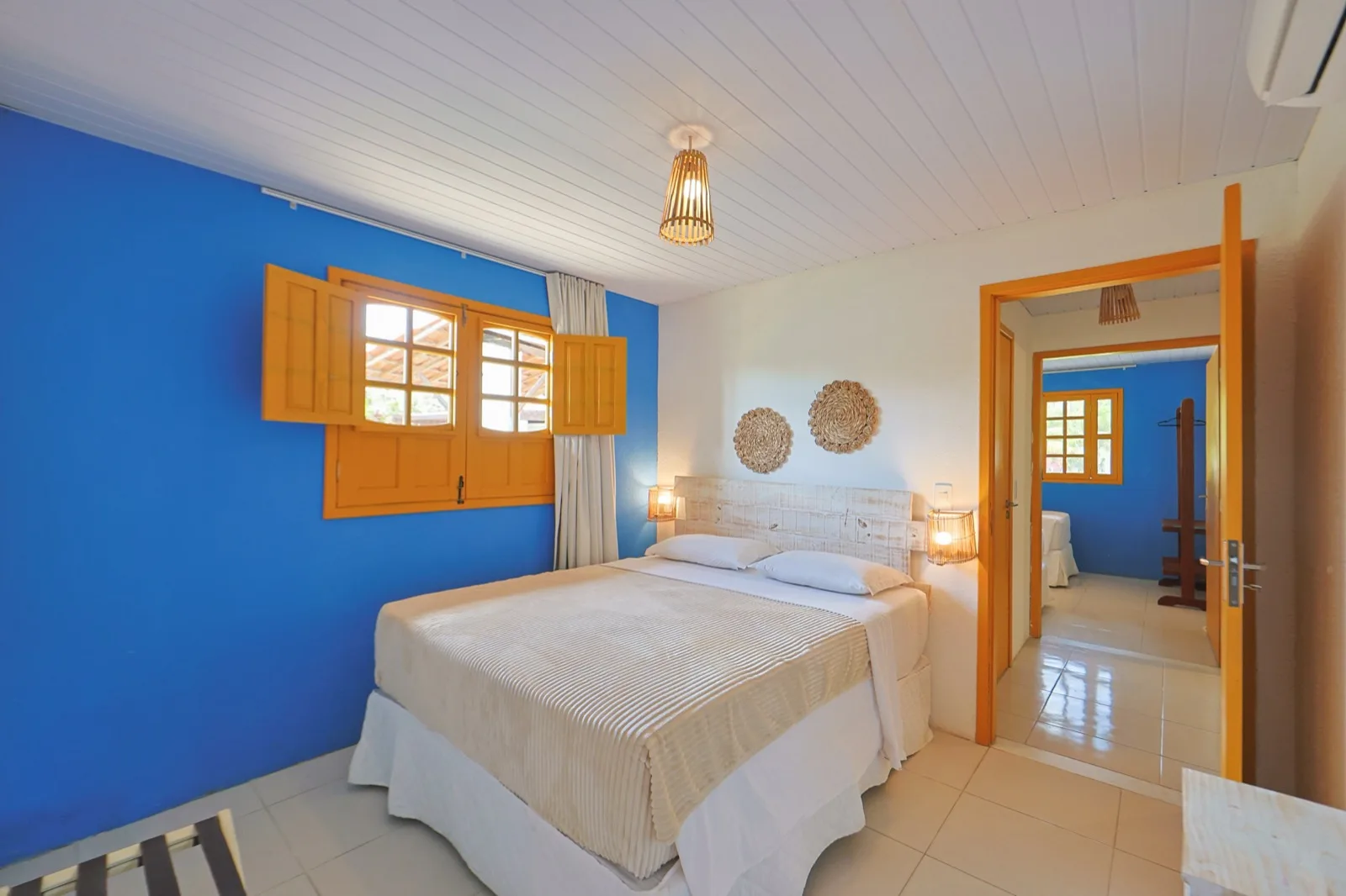 Casa Haras, suíte com parede azul, janela amarela e cama de casal