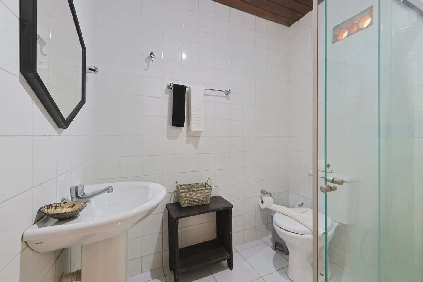 Segundo banheiro com box de vidro, azulejos brancos e detalhes rústicos