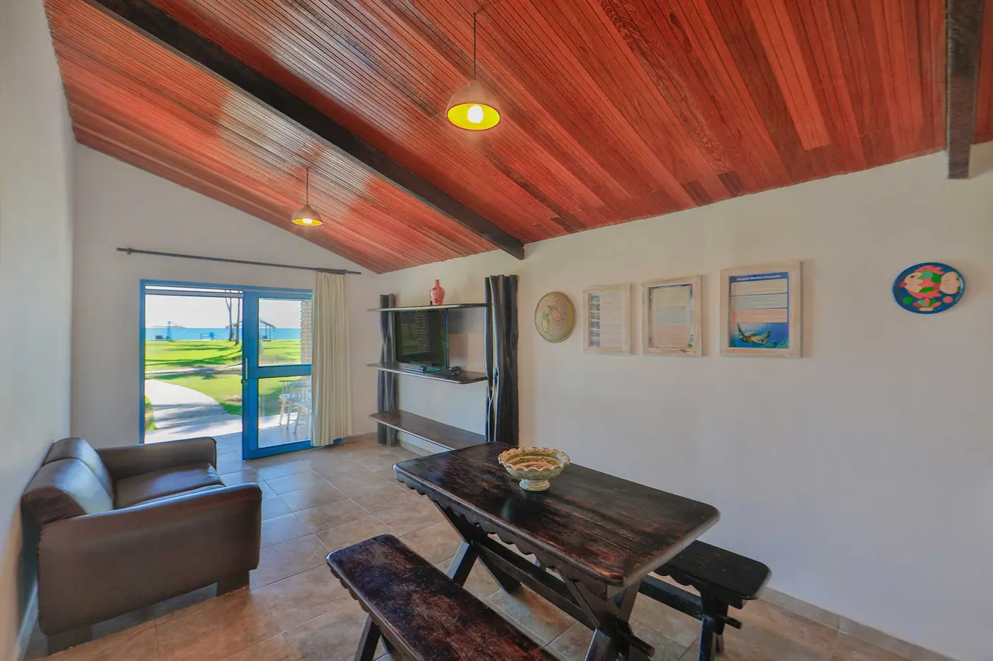 Sala de estar integrada com sofá, mesa rústica e teto de madeira