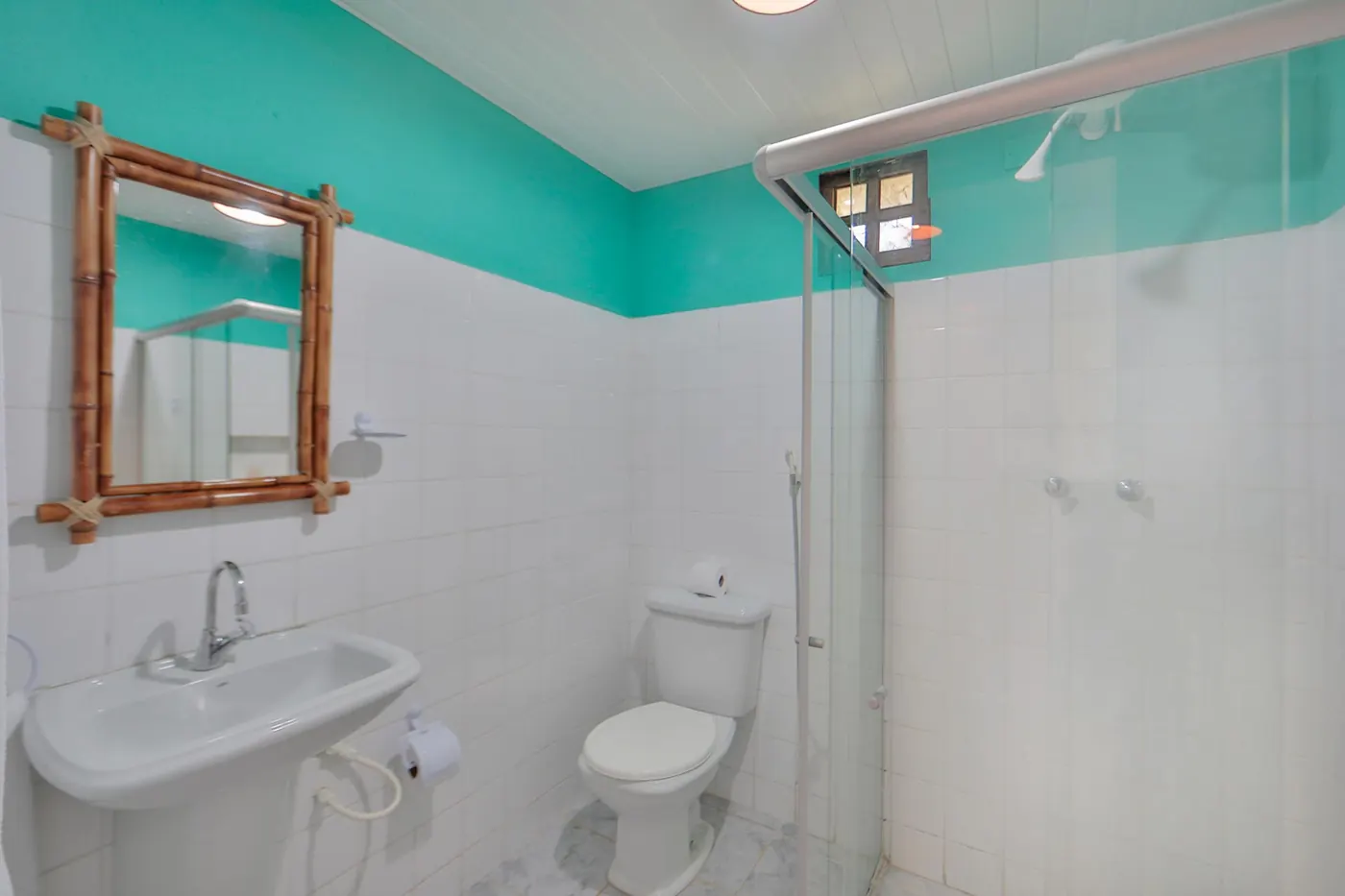 Banheiro com box de vidro, azulejos brancos e detalhes em verde-mar