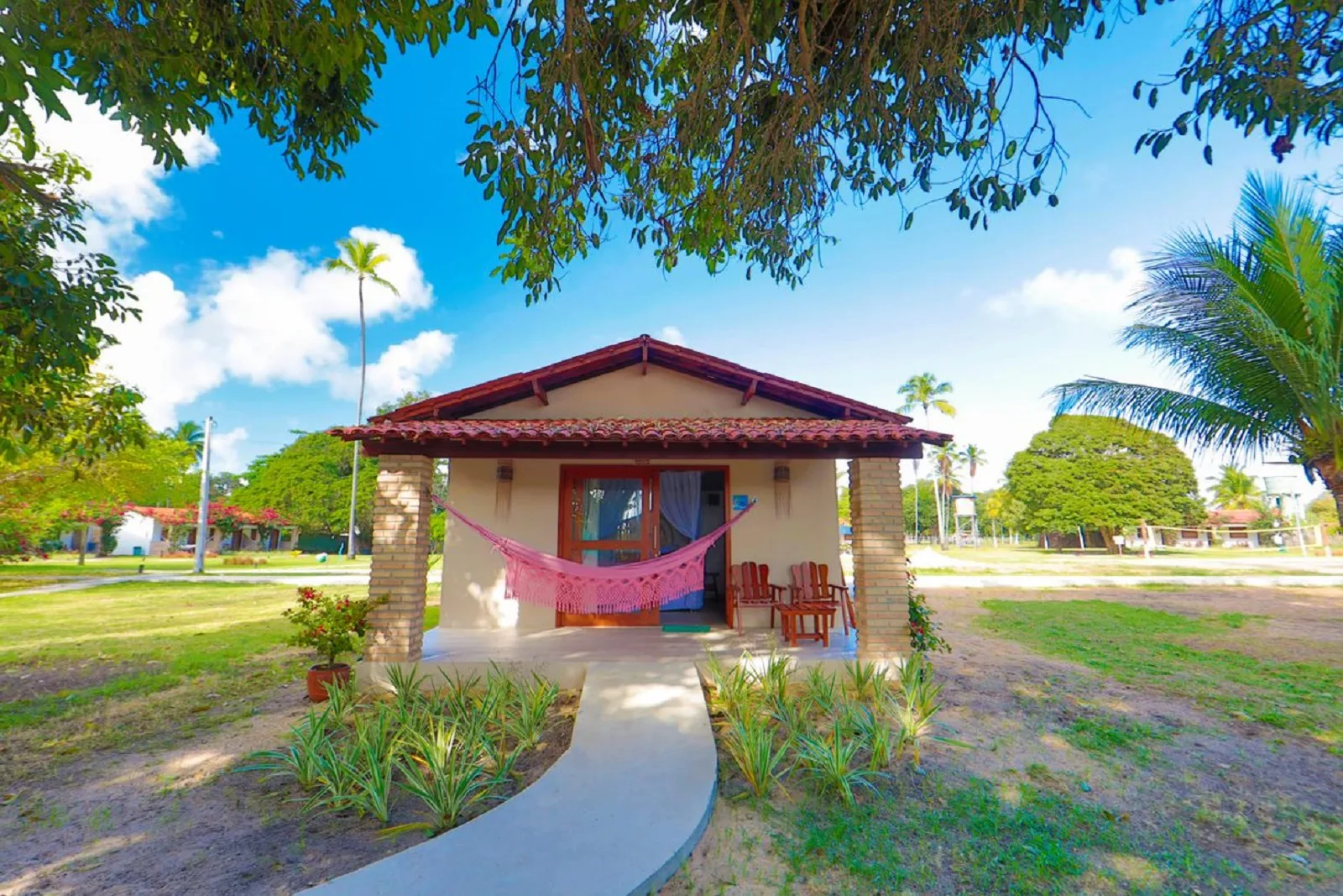 Bangalô Duplo Vista Parcial do Mar, fachada com telhado colonial, rede rosa na varanda e árvore frondosa ao lado