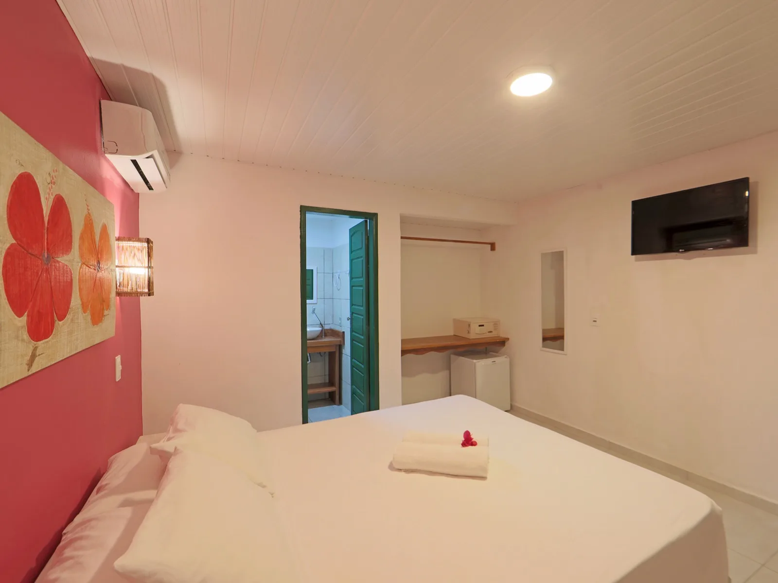 Econômico Sem Vista Mar, quarto de casal com parede rosa, quadro de hibiscos e ar condicionado, porta verde abrindo para o banheiro